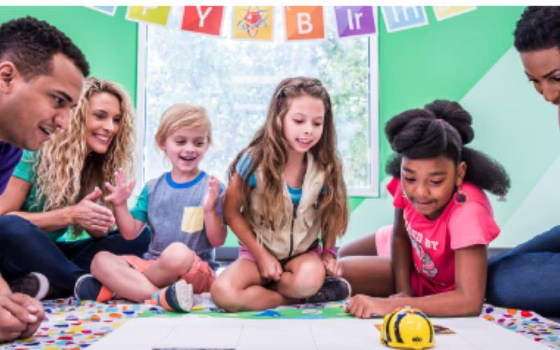Children and adults interacting with a learning robot on a floor grid at a science museum.